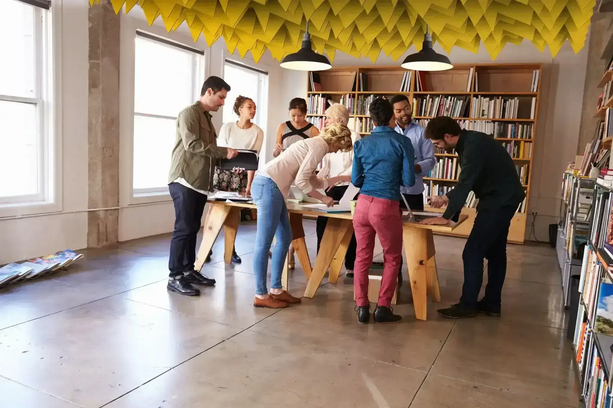 A group of people standing around a wooden table working.